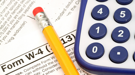 The image shows a close-up of a Form W-4, used for tax purposes, partially visible. A yellow pencil with an eraser is resting on the form, and a blue calculator with large buttons sits nearby, emphasizing the theme of calculating taxes or completing tax documents.